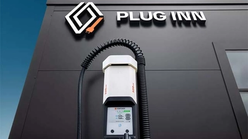 EV fast charger with a coiled cable installed on a dark building facade under the Plug Inn brand sign