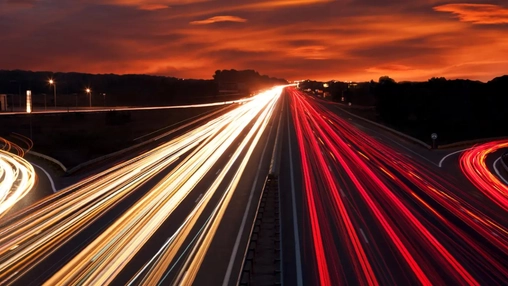 Long-exposure shot of motorway traffic light trails at dusk with a dramatic red sky