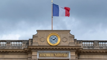 Tricolour flag flying above a neoclassical building with a gold clock on the facade